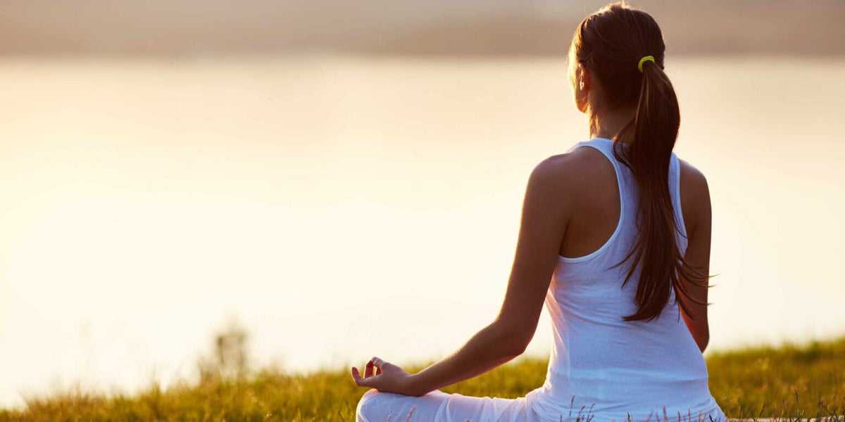 Female sits meditating while overlooking the water