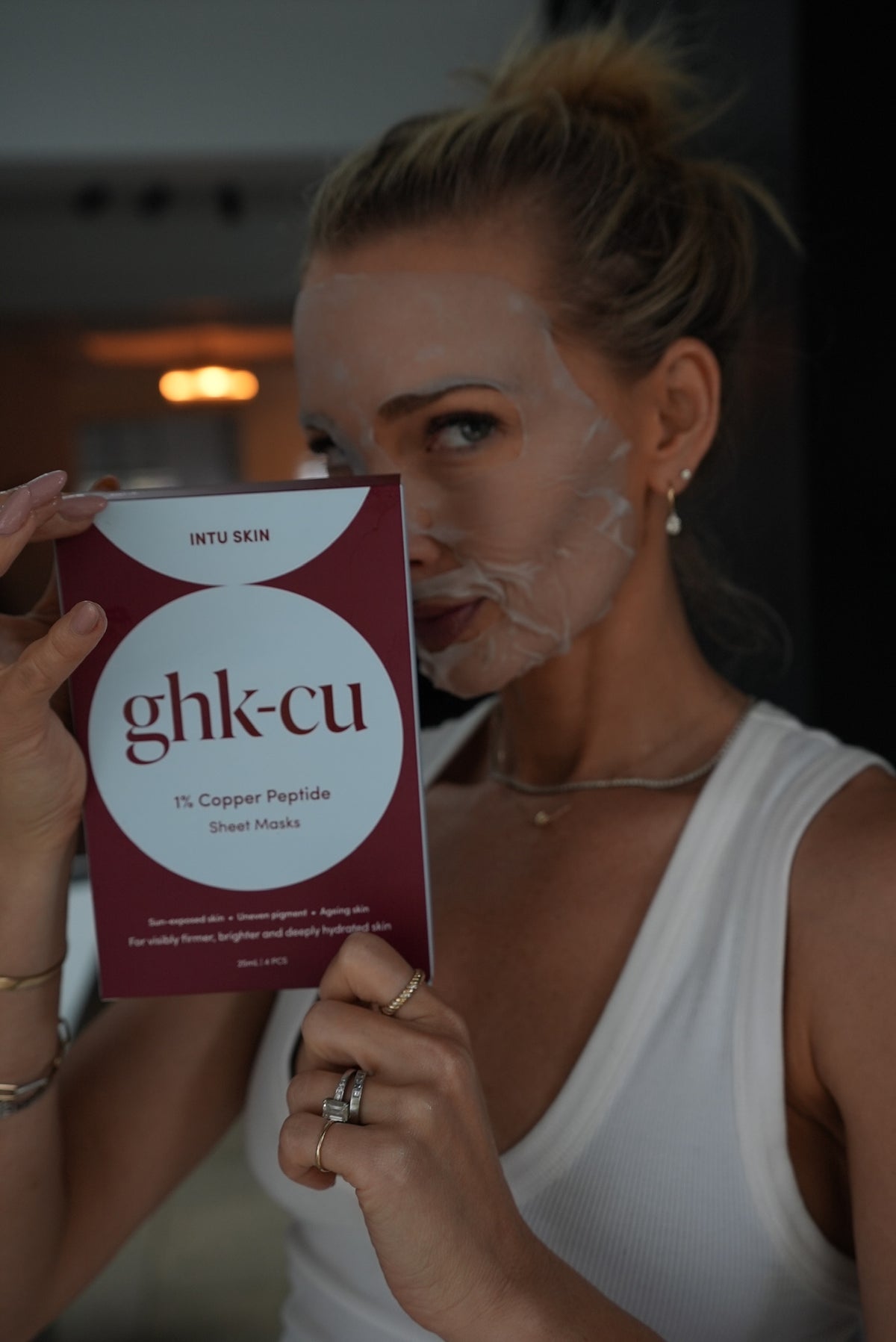Woman wearing an INTU Skin GHK-Cu copper peptide sheet mask, holding the box