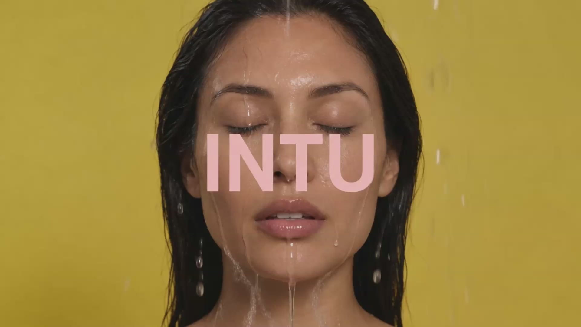 Close-up of a woman's face with water running over her skin and the INTU logo